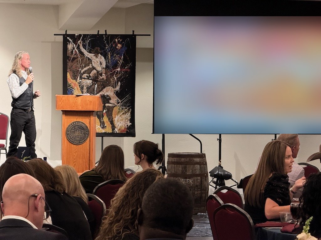 Speaker at the podium beside Michael Israel's bull rider painting during the Guardians Gala auction