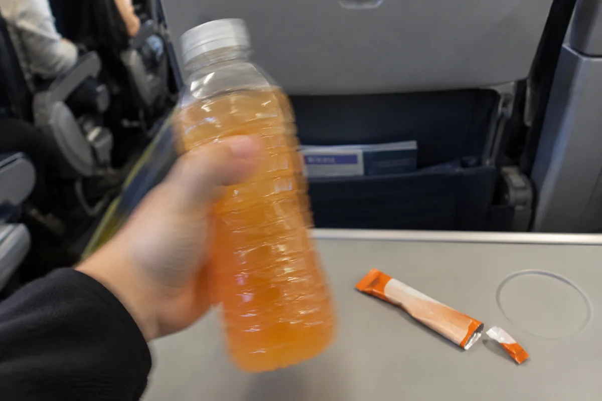 Shaking an electrolyte drink mix inside a plastic water bottle on a plane