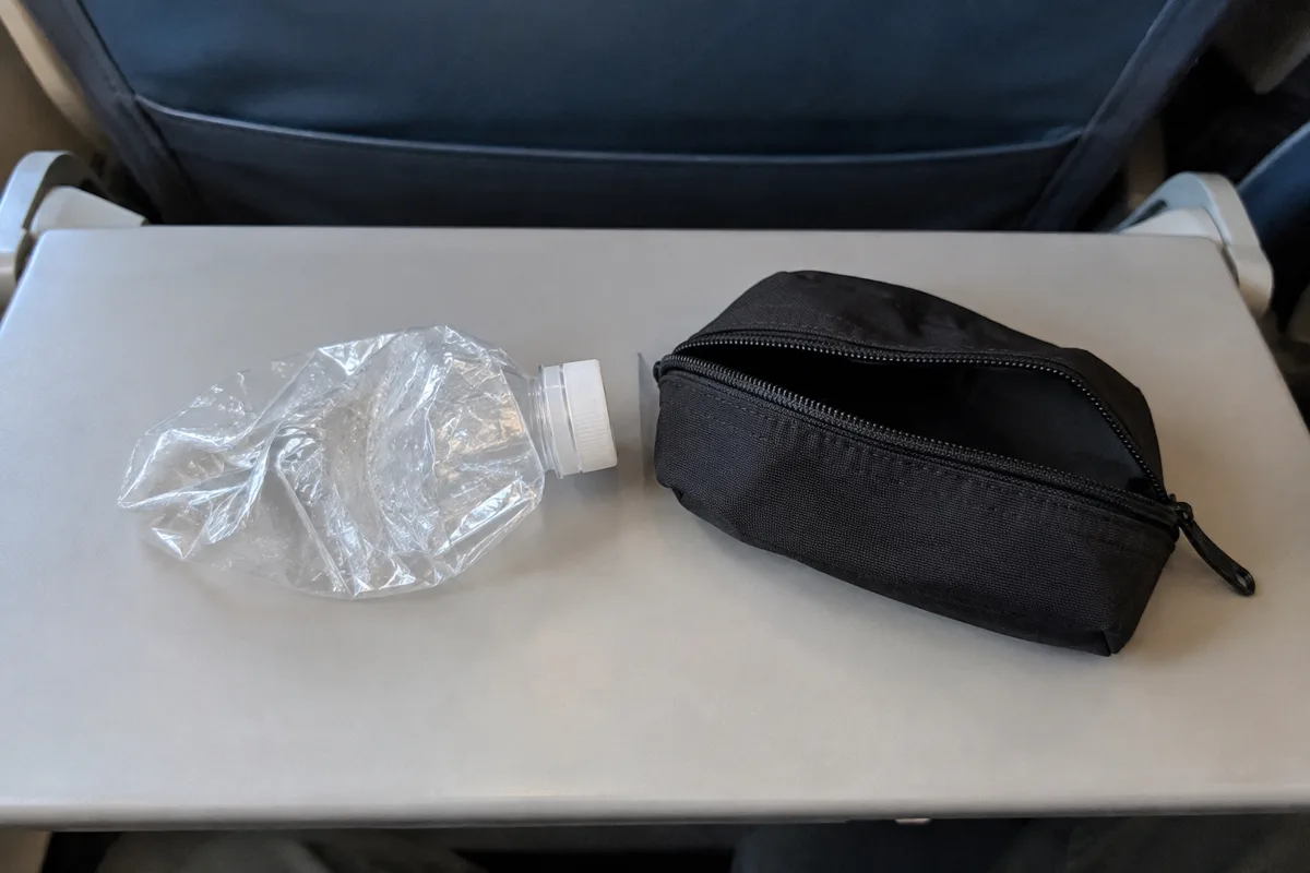 Empty plastic water bottle crushed flat with the cap on, next to a small travel pouch