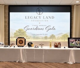 Legacy Land Guardians Gala screen above auction tables