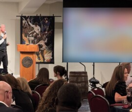 Speaker at the podium beside Michael Israel's bull rider painting during the Guardians Gala auction